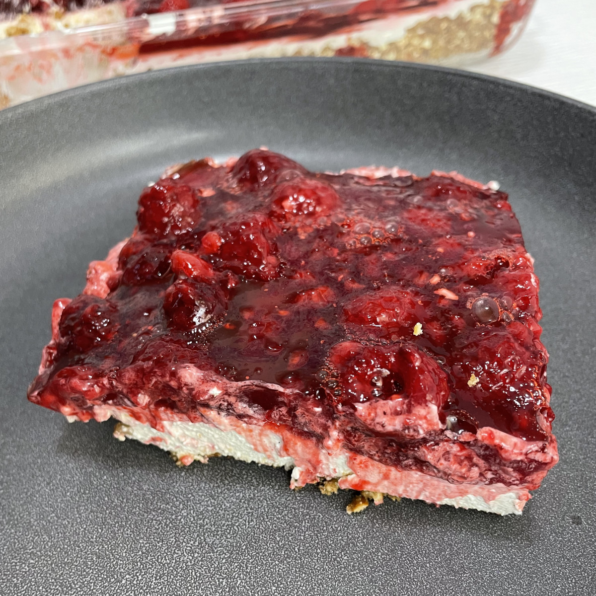A slice of raspberry jello salad sits on a grey plate.
